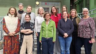 Gruppe Frauen unterschiedlichen Alters steht auf einer Außentreppe vor einem Gebäude mit grün gestrichener Fassade