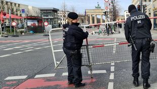 Zwei Polizisten in schwarzer Uniform sichern eine Straßensperre mit Absperrgittern vor dem Brandenburger Tor in Berlin.