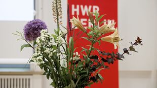 Strauß aus verschiedenen Blumen vor rotem Banner mit weißer Schrift