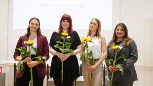 Vier Frauen stehen nebeneinander und halten jeweils eine Sonnenblume vor einem weißen Hintergrund mit der Projektion 'POLITEIA-Preis 2025'