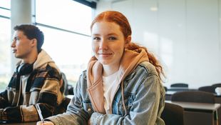 Schülerin sitzt in einem Klassenraum an einem Tisch. 