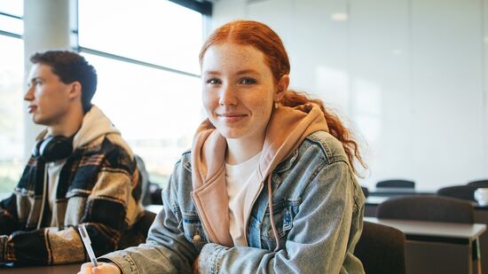 Schülerin sitzt in einem Klassenraum an einem Tisch. 