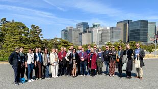 Gruppe von Menschen steht im Freien vor einer Stadt mit Hochhäusern und Bäumen im Hintergrund